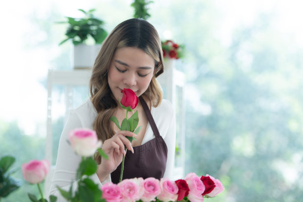 年轻的女花商在花店里闻着一朵红玫瑰图片下载