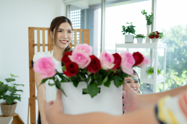 在花店工作的年轻亚洲女花商，她很开心，面带微笑。给顾客送花图片下载