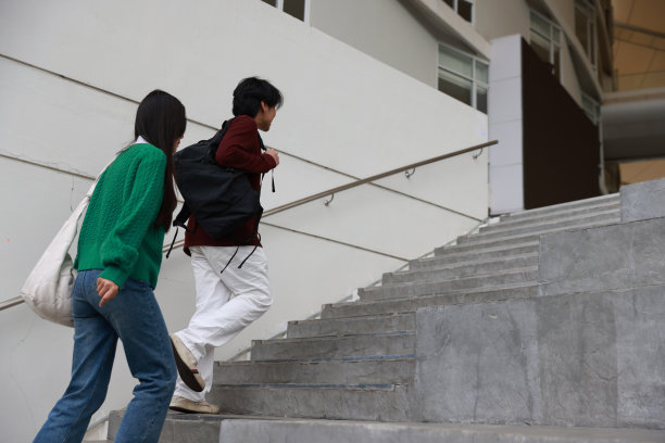 一对夫妇的学生回到学校，他们上楼去大学，手牵着手，和女朋友冲到教室上课。背着大书包，手牵着手去上课。图片下载