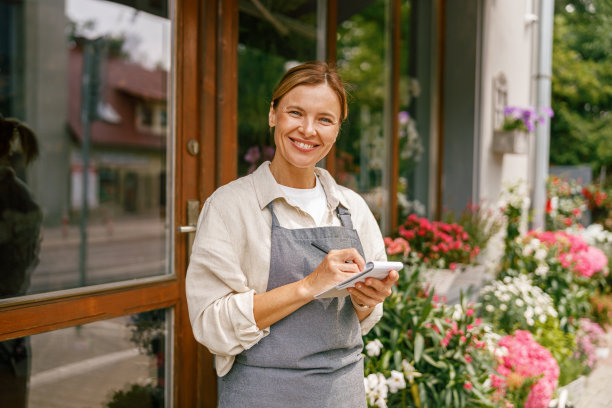 微笑的女花商在花店的笔记本上写订单和客户信息图片下载
