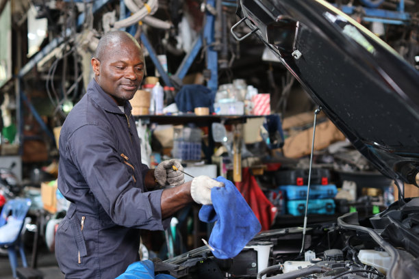 穿着制服的汽车技师在维修站检查、保养汽车。工人检查汽车发动机的机油位。汽车中心维修服务理念。图片下载