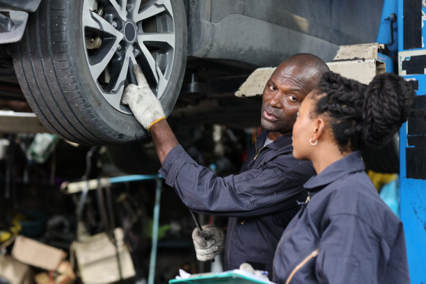 在修车厂站，一组穿制服的汽车机械师拿着剪贴板检查保养升降机服务。工人拿着扳手和修理损坏的车辆。汽车维修服务理念图片下载