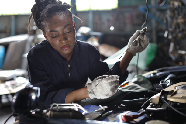 穿着制服的女技师在汽车维修站检查保养汽车。工人检查汽车发动机的机油位。汽车中心维修服务理念。图片下载