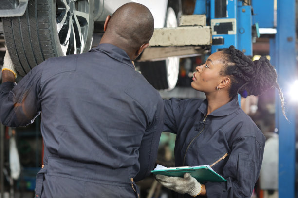 在修车厂站，一组穿制服的汽车机械师拿着剪贴板检查保养升降机服务。工人拿着扳手和修理损坏的车辆。汽车维修服务理念图片下载