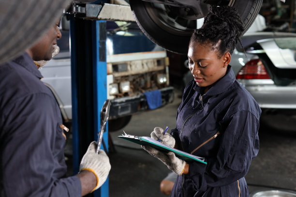 在修车厂站，一组穿制服的汽车机械师拿着剪贴板检查保养升降机服务。工人拿着扳手和修理损坏的车辆。汽车维修服务理念图片下载