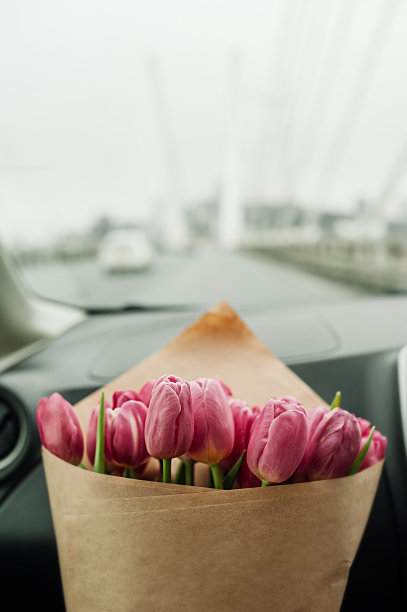 别致的一大束粉红色郁金香用牛皮纸包装在汽车内饰的道路上。花的内容，花的传递，选择性的焦点图片下载
