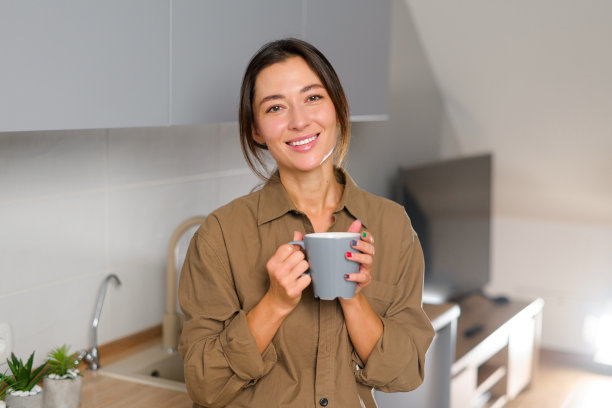 腰部以上肖像的看法，一个美丽的亚洲黑发女孩站在与一杯咖啡在她的手在厨房和微笑图片下载