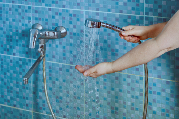 从淋浴喷头喷出的水倒进手掌靠在墙上的蓝色小瓷砖上。图片下载