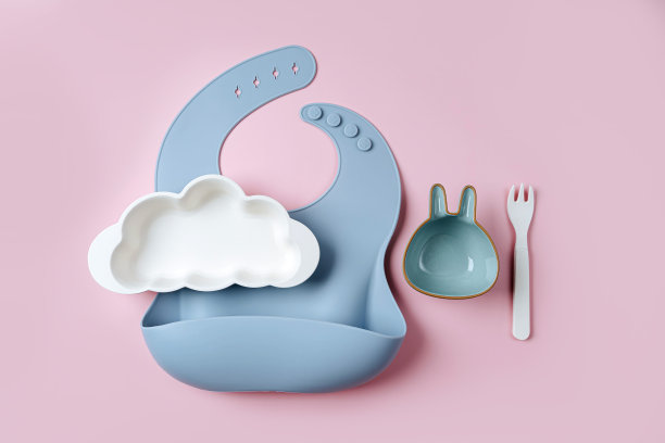 婴儿围兜和盘子的形状在粉红色的背景上的云。婴儿服务。儿童菜单、营养和喂养的概念图片下载
