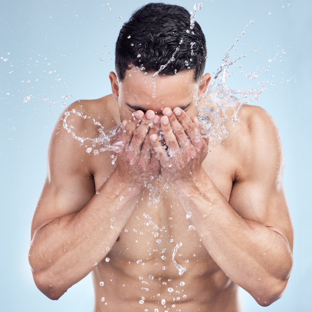英俊的年轻男子在灰色背景的工作室里往脸上泼水图片下载