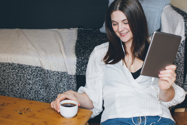 年轻女子在家边视频聊天边喝咖啡。图片下载