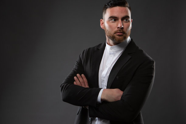 一个野蛮的商人的肖像，没有刮胡子，穿着黑色西装和白色衬衫，在黑暗的背景下摆姿势图片下载