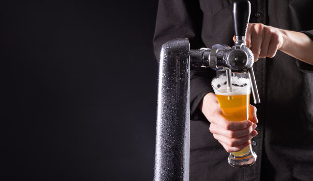 酒保把新鲜的啤酒从龙头倒进一个玻璃杯里，背景是黑色的图片下载