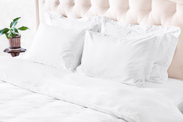 卧室有床，白色寝具和床头柜。白色枕头，羽绒被和羽绒被盒床上米色床头板。图片下载