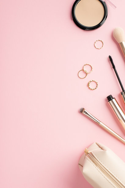 构成美的概念。俯视图垂直照片的金戒指紧凑的粉末化妆刷睫毛膏和化妆包在粉彩粉红色的背景与空白图片下载