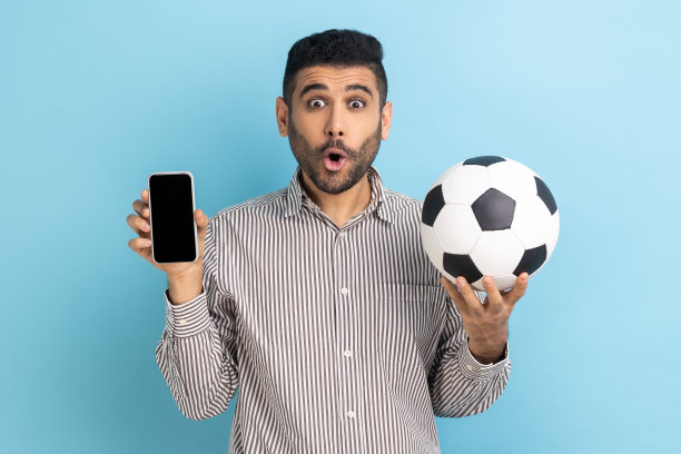 手持足球和空白智能手机，对轻松赢得冠军感到震惊的络腮胡男人图片下载