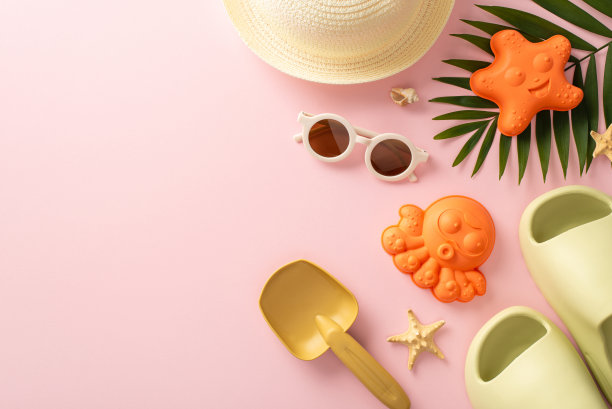 夏天和孩子们在海边旅行的美好回忆。上图为海洋贝壳、海滩玩具、巴拿马帽、拖鞋、太阳镜和棕榈叶，背景为粉红色，带有文字空间图片下载