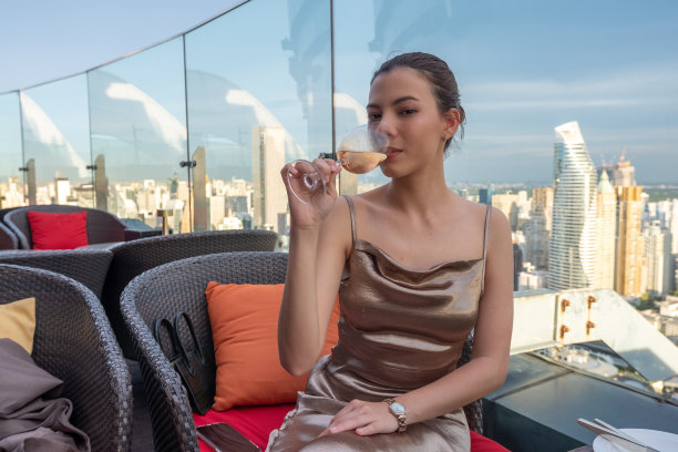 身着金色长裙的优雅年轻女子喝着粉红玫瑰酒。图片下载