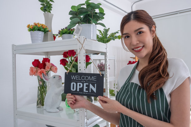 美丽的亚洲花商在自己的店里举着开店的牌子。图片下载