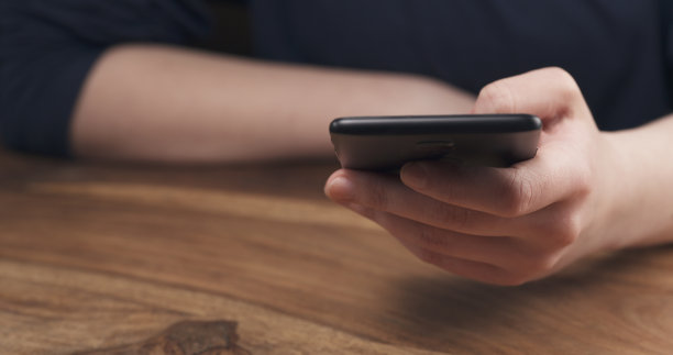 年轻的女青少年手握智能手机坐在桌子旁的特写图片下载