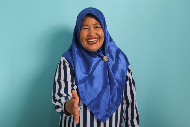 自信的亚洲妇女戴着蓝色的头巾，站在蓝色的背景下，邀请握手。图片下载