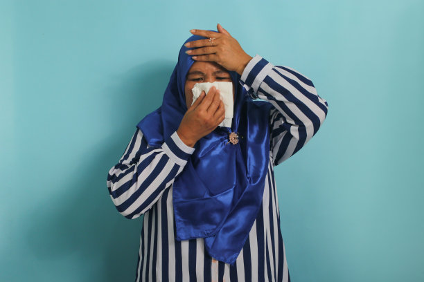 患流感的亚洲妇女戴蓝色头巾打喷嚏，擤鼻子。医疗保健的概念。图片下载