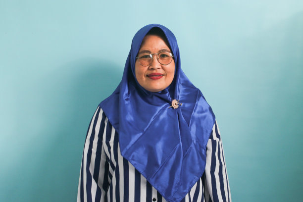 戴着头巾，戴着眼镜的中年亚洲妇女，在蓝色的背景下孤独地看着镜头。图片下载