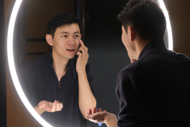 英俊的亚洲年轻男子在镜子前把护肤品涂在脸上图片下载