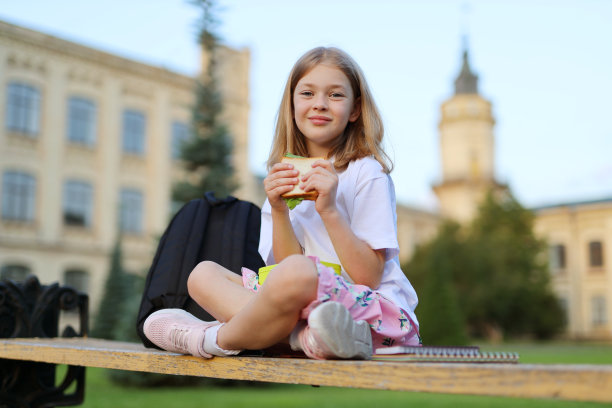 开朗可爱的小女孩，手里拿着三明治，在学校的背景下午休。图片下载