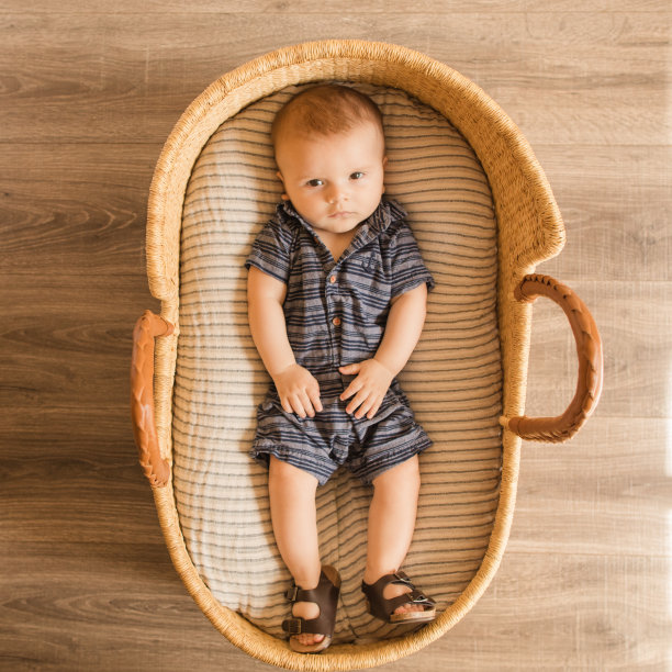 一个21周大的男婴穿着蓝色牛仔装，躺在一个舒适的奶油色条纹棉毯上，在海草摩西篮子图片下载