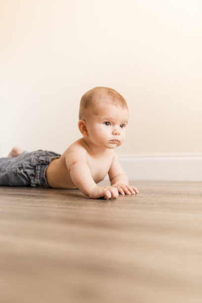 一个24周大的男婴穿着蓝色牛仔牛仔裤和没有衬衫，躺在一个明亮的家里的木地板上图片下载