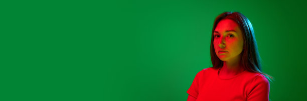 在霓虹灯的绿色背景下，穿着红色衣服的年轻女孩严肃地看着相机的肖像图片下载