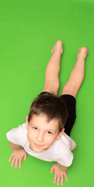 小男孩在绿色瑜伽垫上做体操。居家健身概念图片下载