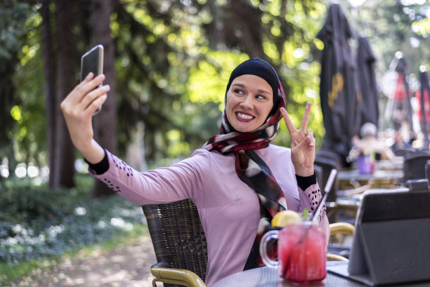 一名穆斯林妇女一边喝着果汁一边自拍。图片下载