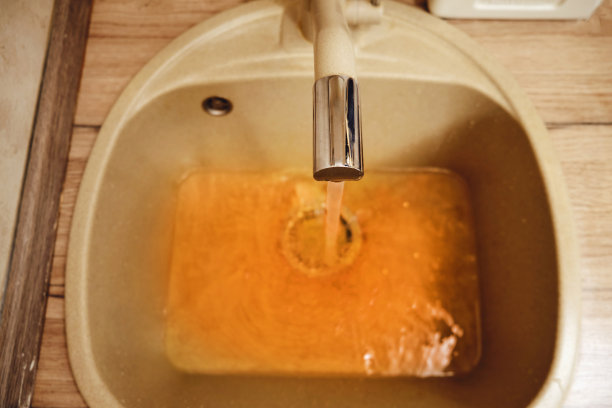 生锈的水从水龙头流入家庭厨房的水槽。在不卫生的浴室里，生锈的水龙头滴着脏水。图片下载