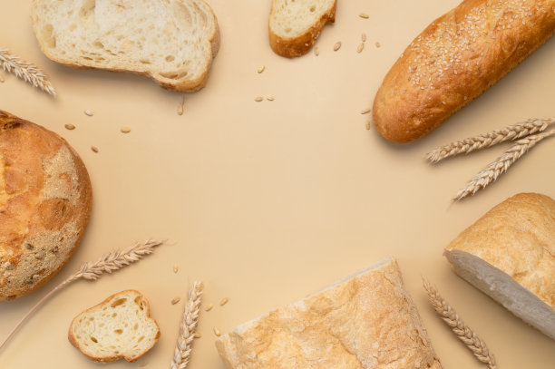 面包的背景。新鲜的白小麦面包，圆形的经典，意大利面包，法国法棍面包，麦穗和谷物在米色背景平放置顶部视图。做面包，烘焙，健康食品。光模型图片下载