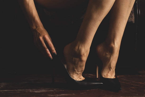 女孩穿着黑色的高跟鞋站在家里的木制旧地板上，脚踩在地板上，鞋子图片下载