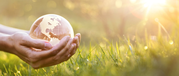 在草地和阳光的背景下，女性手中的绿色星球图片下载