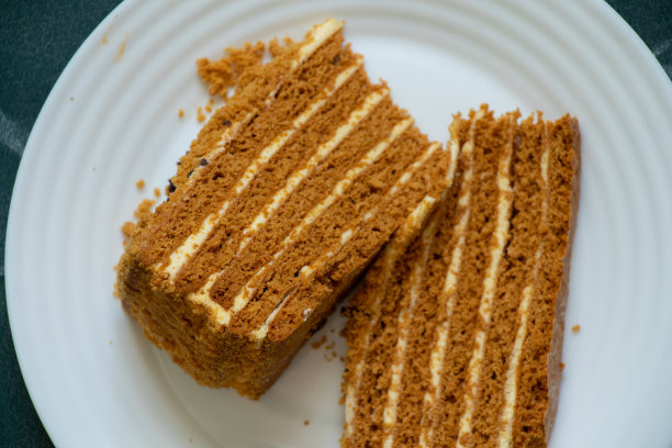 一块自制的蜂蜜蛋糕，放在深绿色背景的白色盘子上图片下载