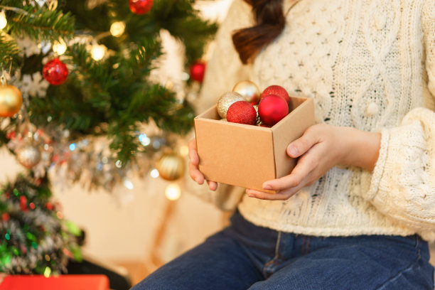 圣诞概念，年轻的亚洲妇女戴着圣诞老人的帽子，拿着圣诞球的盒子装饰图片下载