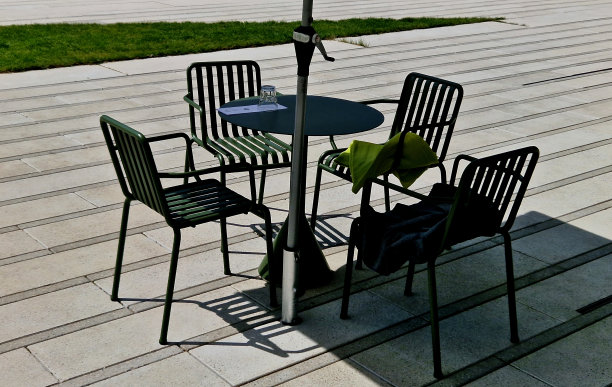 在一次工作会议上，行政区域人行道上的咖啡馆露台。黑色网椅和方形木桌。一个装咖啡的纸杯和一部手机。牛角面包在盘子里。脚在图片下载