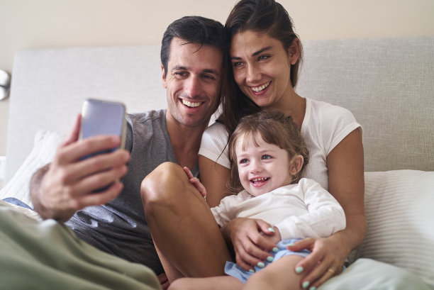 快乐的年轻西班牙夫妇与蹒跚学步的孩子与智能手机自拍图片下载
