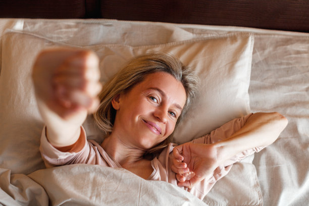 快乐的中年妇女坐在床上伸展双臂图片下载