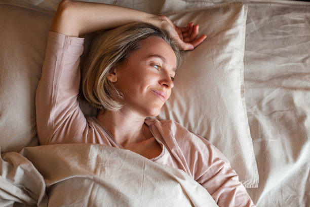 快乐的中年妇女坐在床上伸展双臂图片下载