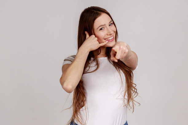 肖像美丽的棕色头发的女人站在呼叫手势，看着和指向相机。图片下载