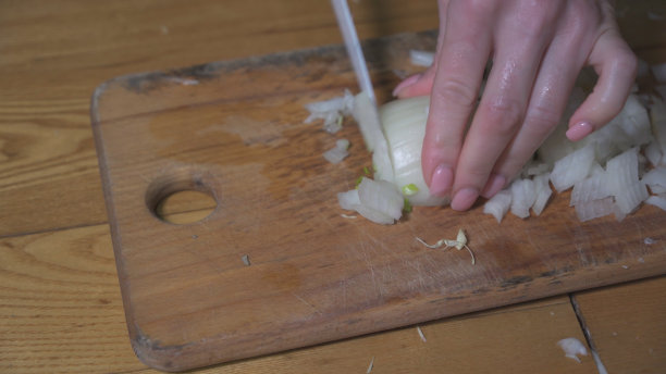 女人的手在木板上切洋葱。一个女人在准备做一道菜的配料。图片下载