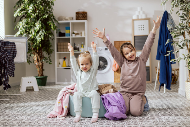 可爱的小女孩坐在洗衣房里。金发女孩在一碗衣服里玩。姐妹们在做家务，在一起消磨时间，高兴地举手图片下载