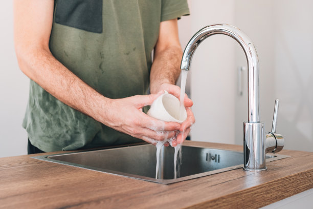 一名男子在厨房水槽边洗咖啡杯图片下载