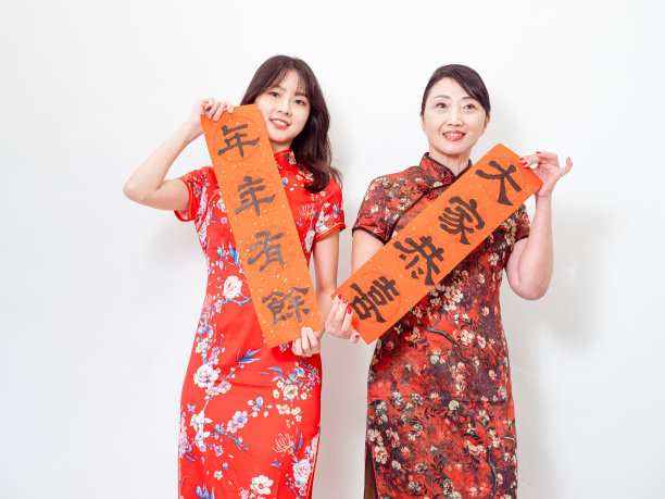 亚洲妇女都穿着传统的旗袍旗袍举行中国的节日对联庆祝新年，在白色的背景上有“愿年年有余”的意思。图片下载