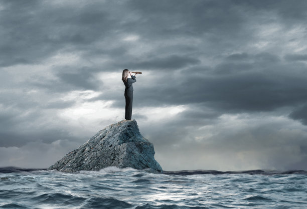 女商人站在海洋的岩石上通过望远镜看图片下载